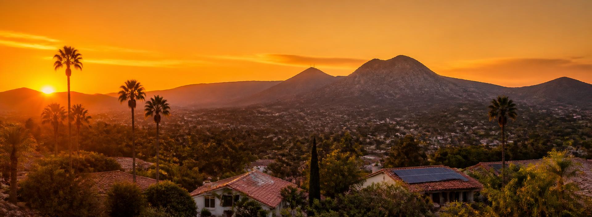 El Cajon valley at golden hour with silhouetted mountains, palm trees, and Spanish tile rooftops with solar panels catching the last sun